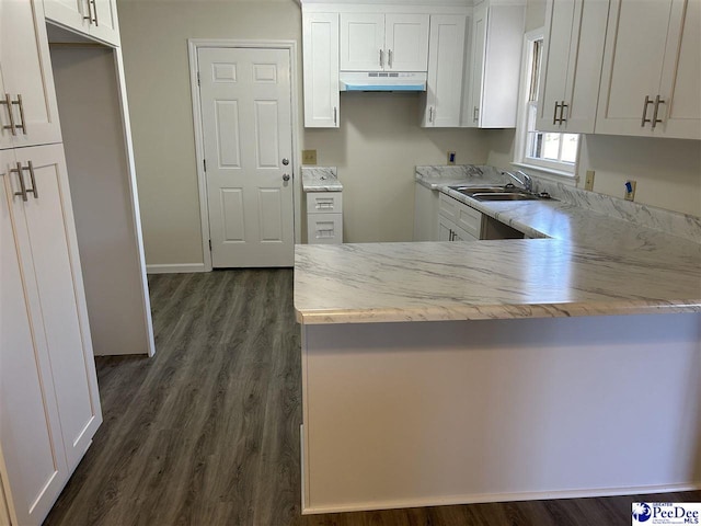 kitchen featuring dark wood finished floors, a peninsula, a sink, white cabinets, and under cabinet range hood