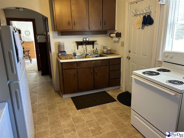 kitchen featuring white appliances, dark brown cabinetry, and sink