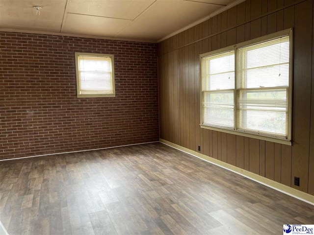 unfurnished room with crown molding, dark hardwood / wood-style floors, and brick wall