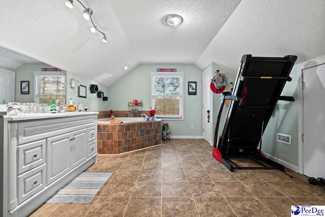 bathroom featuring lofted ceiling, a wealth of natural light, tiled bath, and a textured ceiling