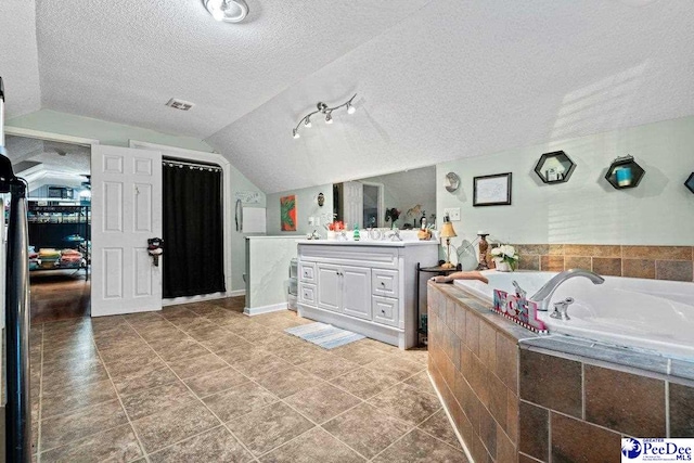 bathroom featuring vanity, lofted ceiling, tiled bath, and a textured ceiling