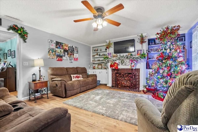 living room with crown molding, ceiling fan, wood-type flooring, a textured ceiling, and a brick fireplace