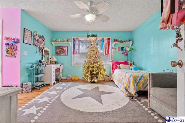 bedroom with ceiling fan, wood-type flooring, and a textured ceiling