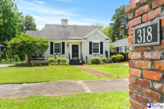 318 Mcleod St, Florence, SC 29501 - view of front of house featuring a front yard, a chimney, roof with shingles, and brick siding