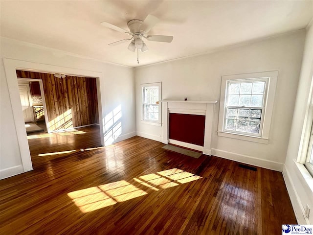 unfurnished living room featuring dark wood-type flooring, ceiling fan, plenty of natural light, and ornamental molding