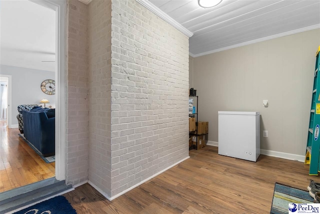 interior space featuring brick wall, baseboards, crown molding, and wood finished floors