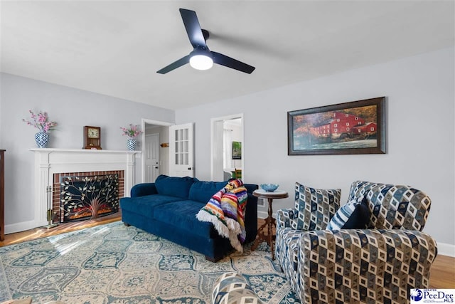 living room with ceiling fan, baseboards, a brick fireplace, and wood finished floors