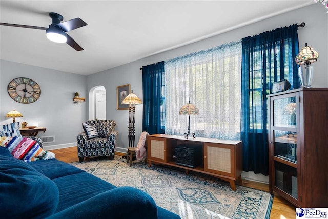 living area with wood finished floors, visible vents, a ceiling fan, arched walkways, and baseboards