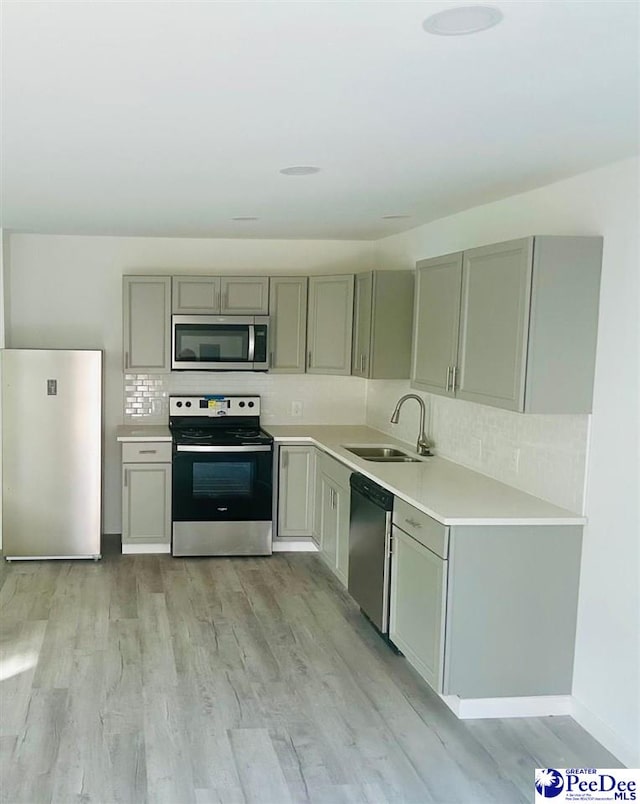 kitchen with sink, gray cabinetry, tasteful backsplash, light hardwood / wood-style flooring, and appliances with stainless steel finishes