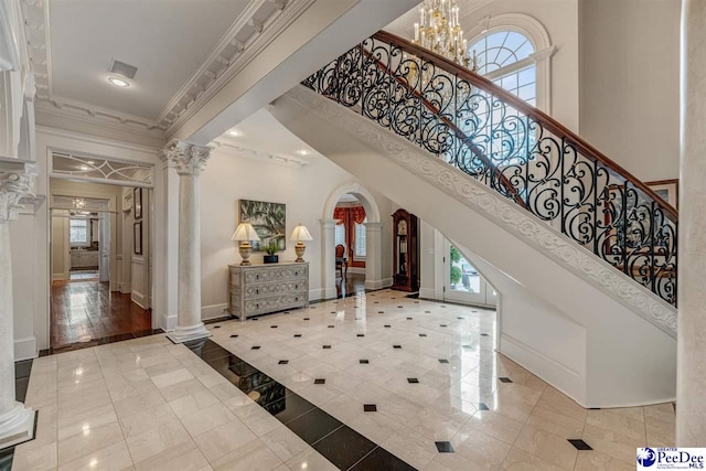 foyer entrance featuring decorative columns, crown molding, a high ceiling, and a chandelier