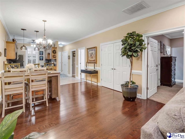 kitchen featuring dark wood-type flooring, an inviting chandelier, hanging light fixtures, ornamental molding, and a kitchen breakfast bar