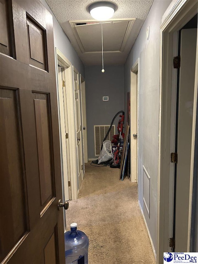 corridor with carpet flooring, a textured ceiling, visible vents, and attic access