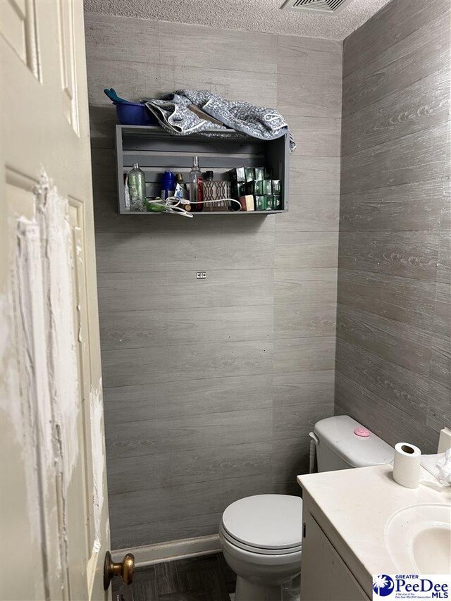 half bath with toilet, wood walls, and vanity