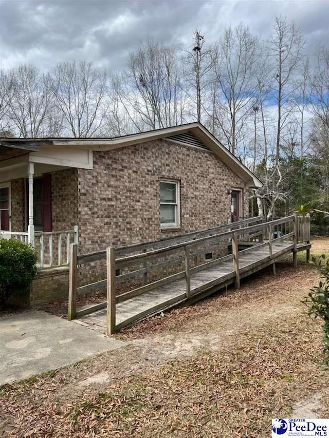 view of side of property featuring brick siding, covered porch, and fence