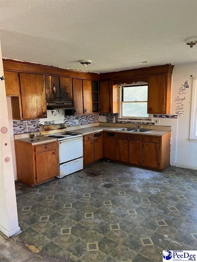 kitchen with brown cabinetry, white range with electric cooktop, a sink, under cabinet range hood, and stone finish flooring