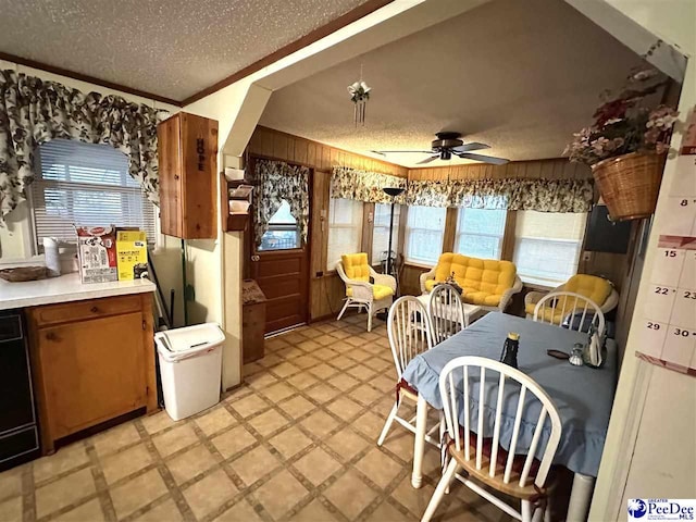 kitchen featuring ceiling fan, ornamental molding, a textured ceiling, and wood walls