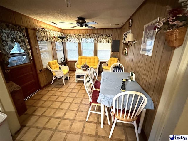 dining space with ceiling fan, wooden walls, and a textured ceiling