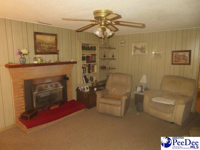 sitting room featuring a brick fireplace, a textured ceiling, ceiling fan, and carpet