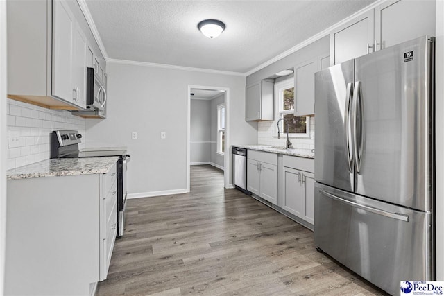 kitchen with stainless steel appliances, ornamental molding, light stone countertops, and light hardwood / wood-style floors