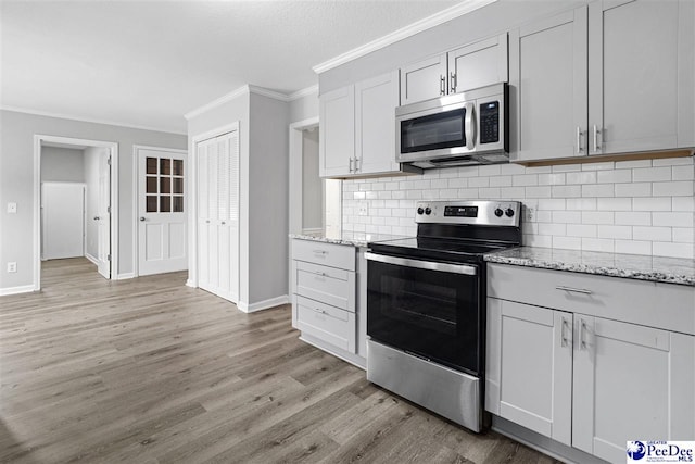 kitchen with light hardwood / wood-style flooring, backsplash, stainless steel appliances, light stone countertops, and ornamental molding