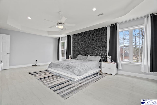 bedroom with a raised ceiling, multiple windows, baseboards, and visible vents