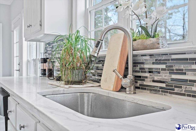 room details with light stone counters, decorative backsplash, white cabinetry, and a sink