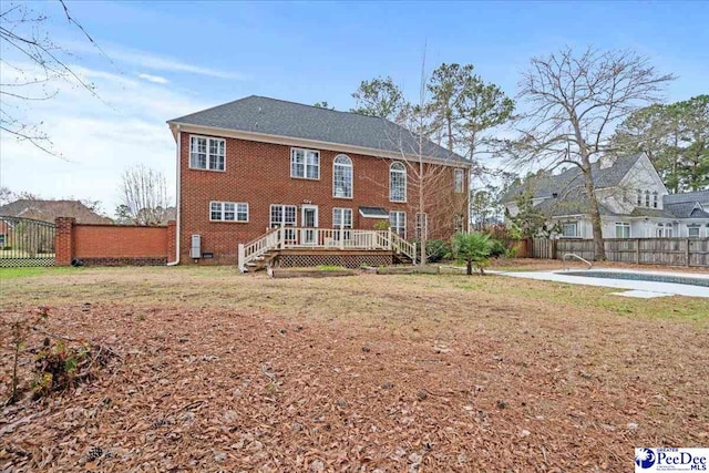 back of house with a lawn, a deck, a fenced backyard, a fenced in pool, and brick siding