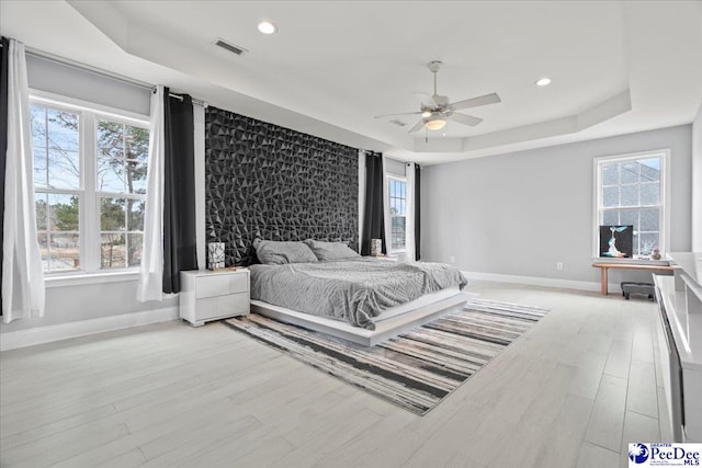 bedroom featuring a raised ceiling, light wood-style floors, visible vents, and baseboards