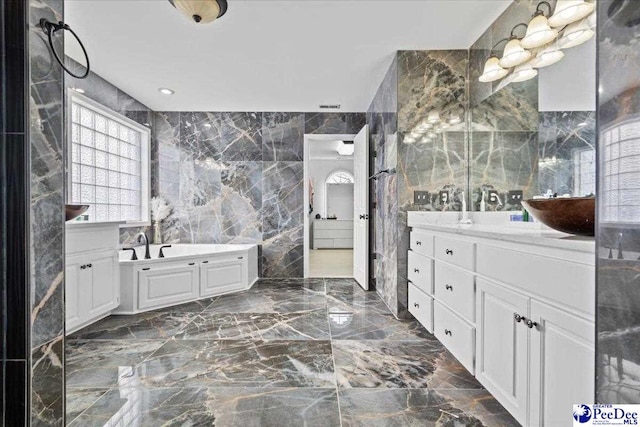 bathroom featuring marble finish floor, tile walls, a garden tub, and two vanities