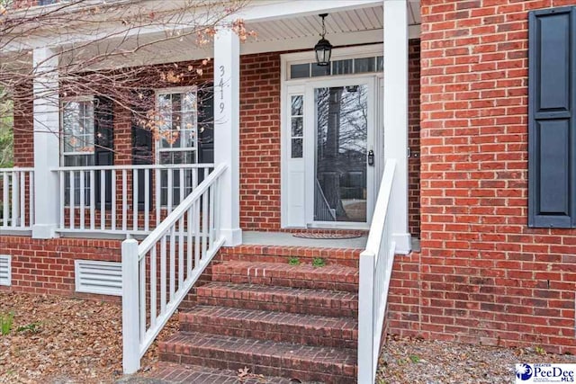 view of exterior entry with brick siding and a porch