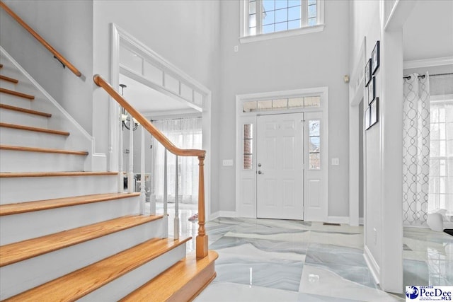 entrance foyer with marble finish floor, a high ceiling, stairs, and baseboards