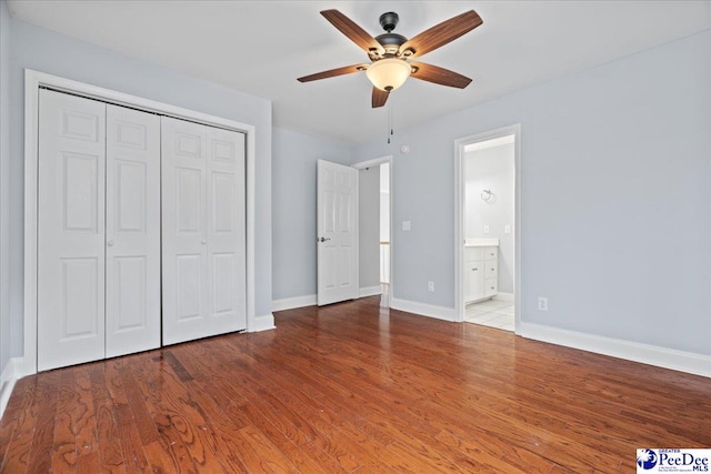 unfurnished bedroom featuring ceiling fan, baseboards, wood finished floors, a closet, and ensuite bath