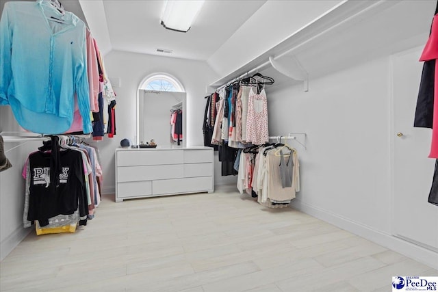 walk in closet with light wood finished floors, visible vents, and lofted ceiling