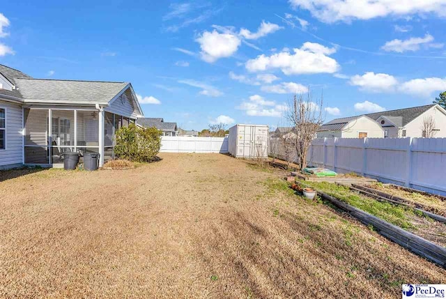 view of yard with an outbuilding, a fenced backyard, a storage shed, a sunroom, and a garden