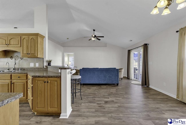 kitchen with a breakfast bar area, lofted ceiling, open floor plan, a sink, and wood finished floors