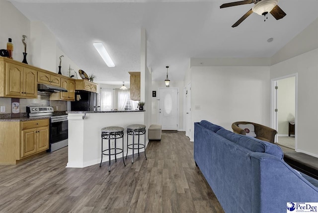 kitchen with under cabinet range hood, a breakfast bar, open floor plan, freestanding refrigerator, and stainless steel range with electric stovetop