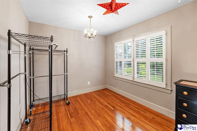 unfurnished bedroom with wood finished floors, a chandelier, and baseboards