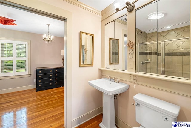 bathroom featuring wood finished floors, tiled shower, baseboards, toilet, and a chandelier