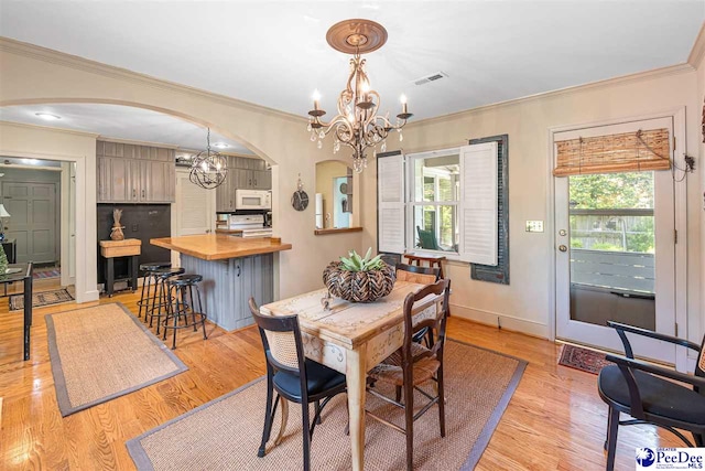 dining room with a chandelier, arched walkways, plenty of natural light, crown molding, and light wood finished floors