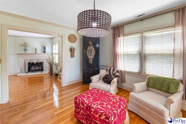 sitting room featuring a fireplace with raised hearth, baseboards, ornamental molding, and wood finished floors