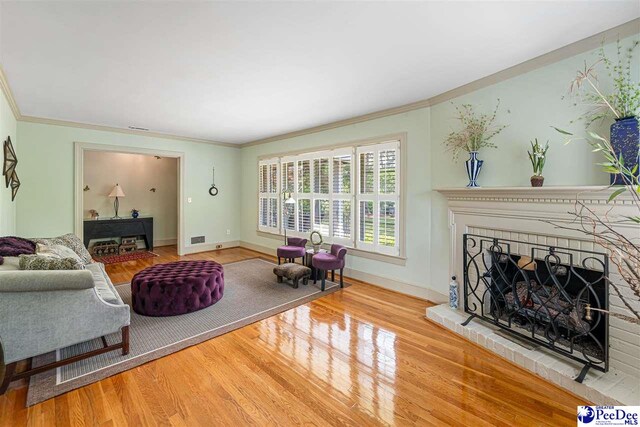 living room with wood finished floors, ornamental molding, a brick fireplace, and baseboards