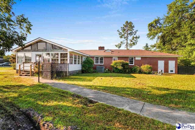 ranch-style home with central air condition unit, brick siding, a front yard, and a sunroom