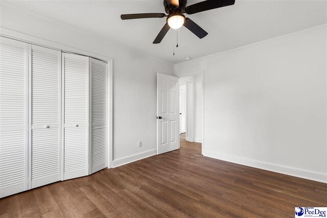 unfurnished bedroom featuring wood finished floors, baseboards, ceiling fan, a closet, and crown molding