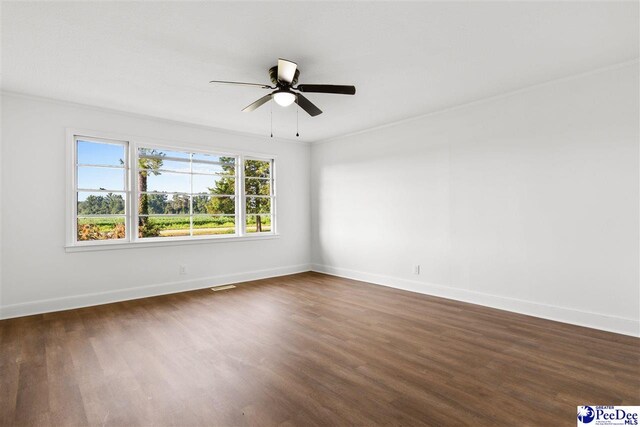 spare room with visible vents, ornamental molding, a ceiling fan, dark wood finished floors, and baseboards