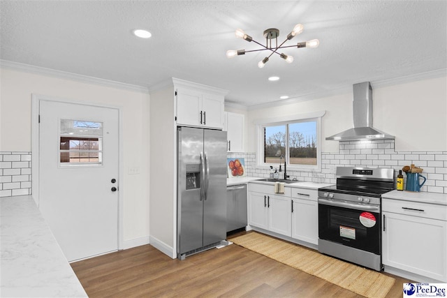 kitchen with a sink, appliances with stainless steel finishes, light wood-style flooring, and wall chimney range hood