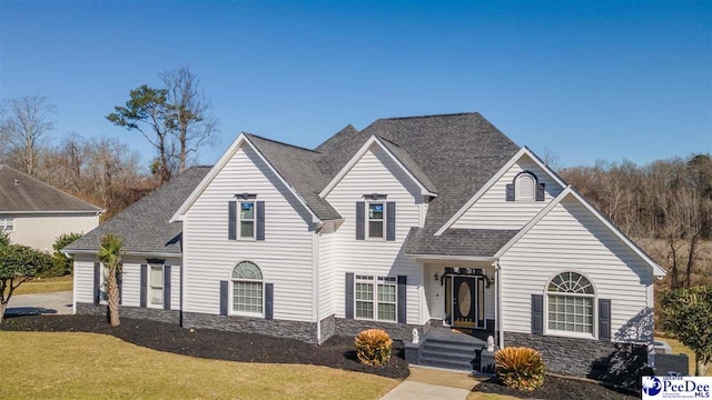 traditional-style home with a front lawn, stone siding, and a shingled roof