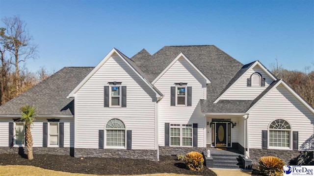 traditional-style home featuring stone siding and a shingled roof