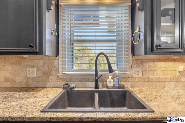 kitchen featuring decorative backsplash, light countertops, glass insert cabinets, and a sink