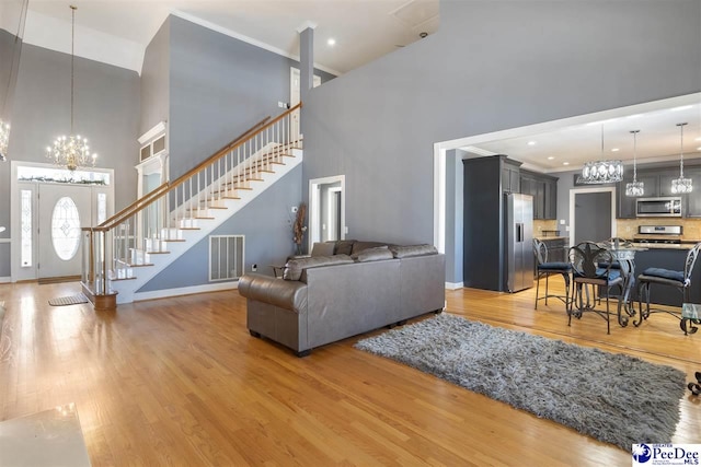 living room featuring stairway, visible vents, light wood-style flooring, ornamental molding, and a notable chandelier