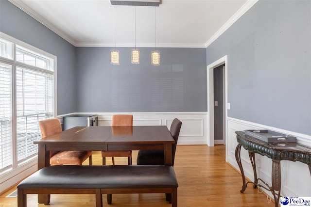 dining room with a wainscoted wall, light wood-type flooring, and ornamental molding